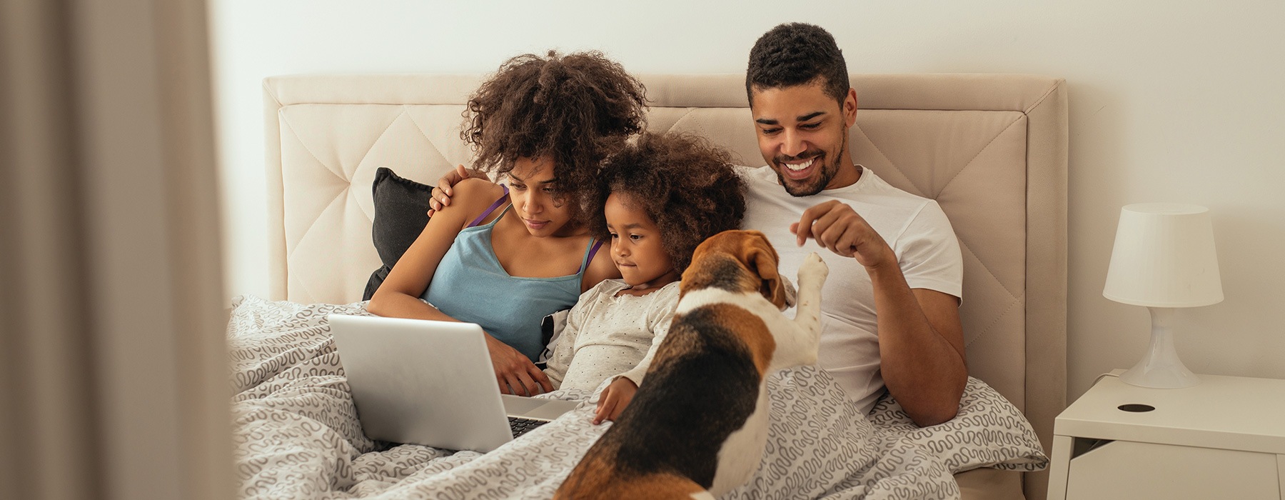 lifestyle image of a family sitting in a bed while watching something online